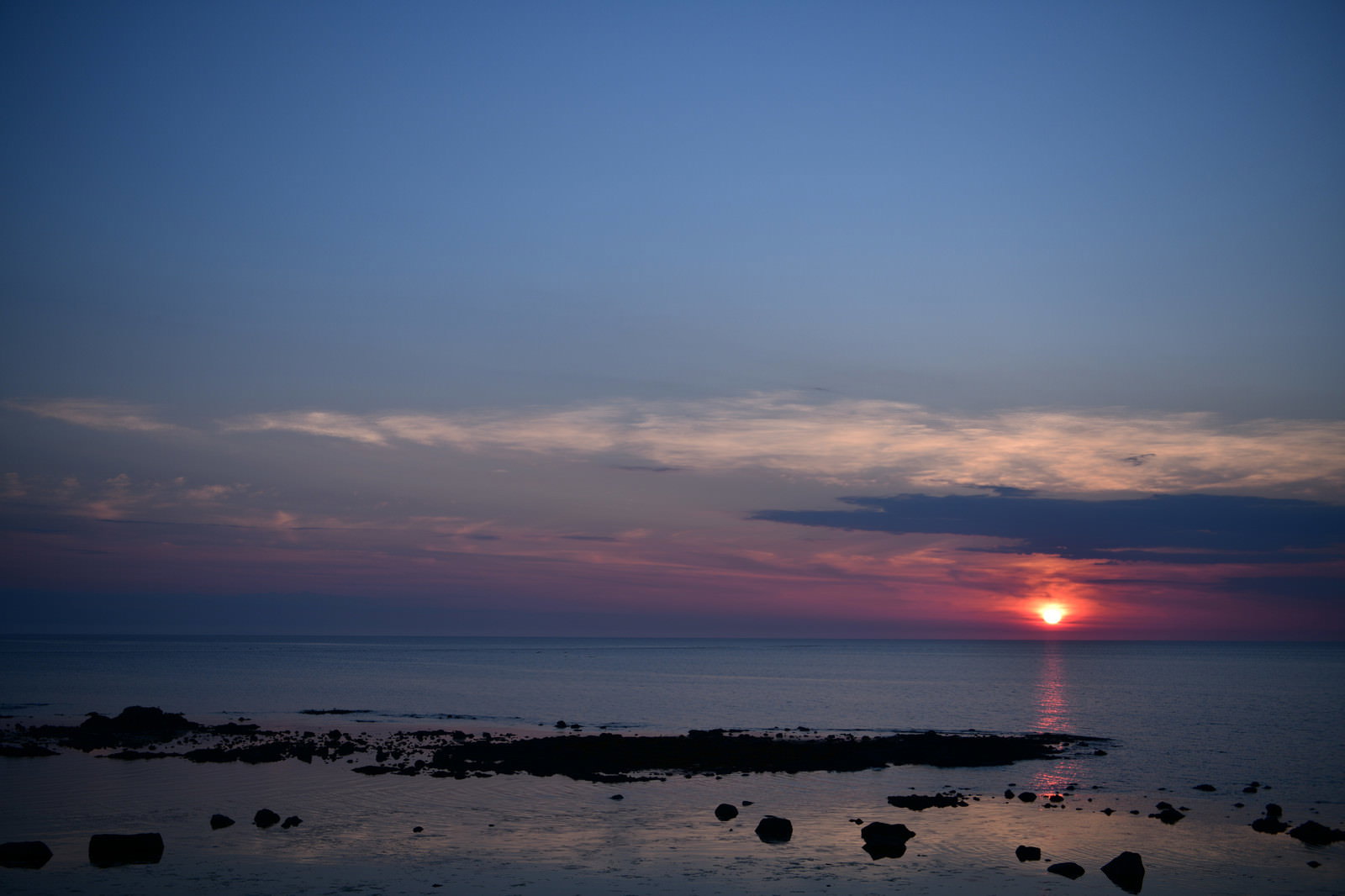 青い海の水平線に沈む夕日と色とりどりの雲が広がる夕焼け空