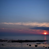 青い海に沈むオレンジ色の太陽の夕日、ピンク色の雲と水平線の写真