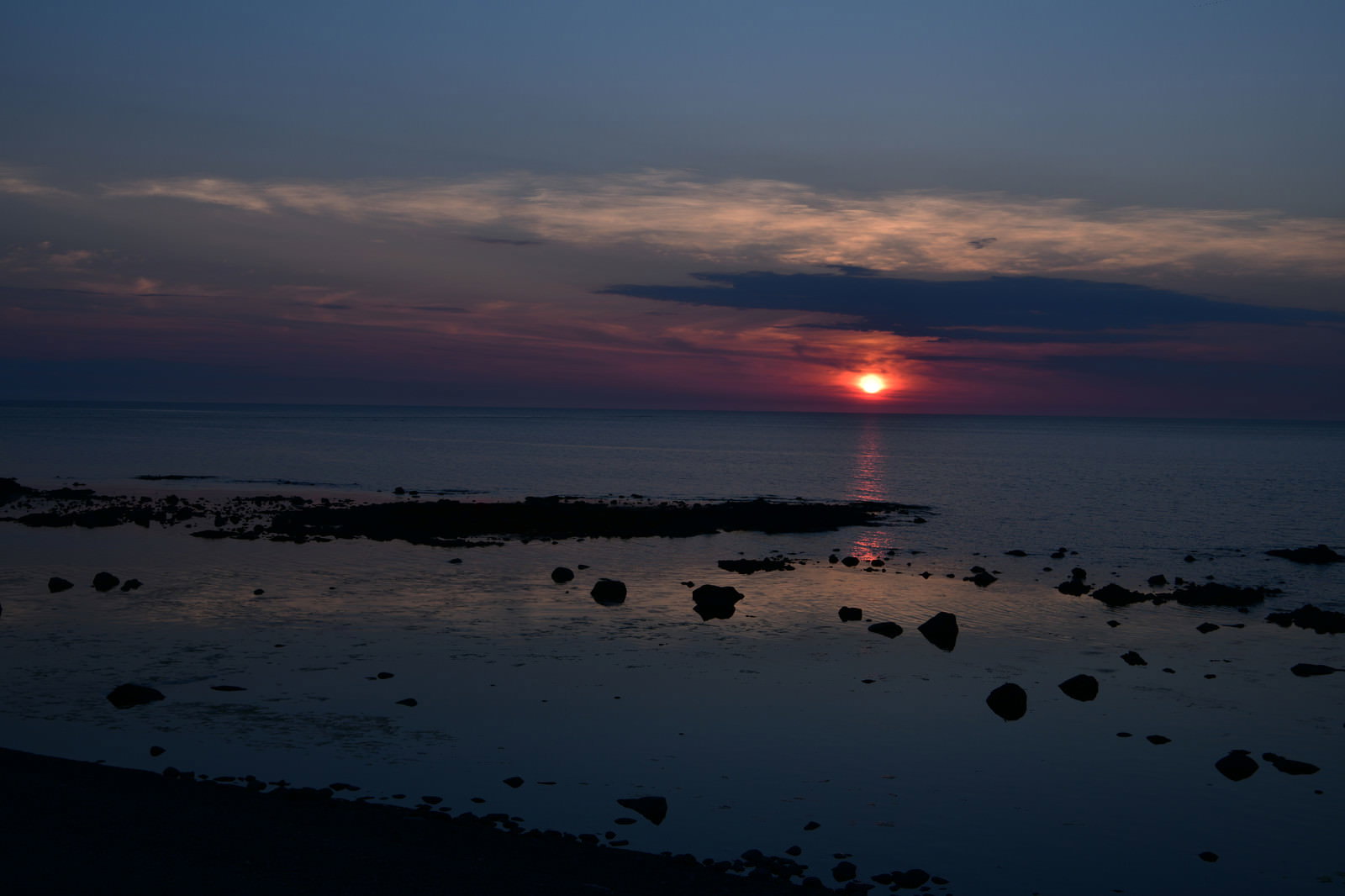 水平線に沈む夕日が海面を赤く染める夕景
