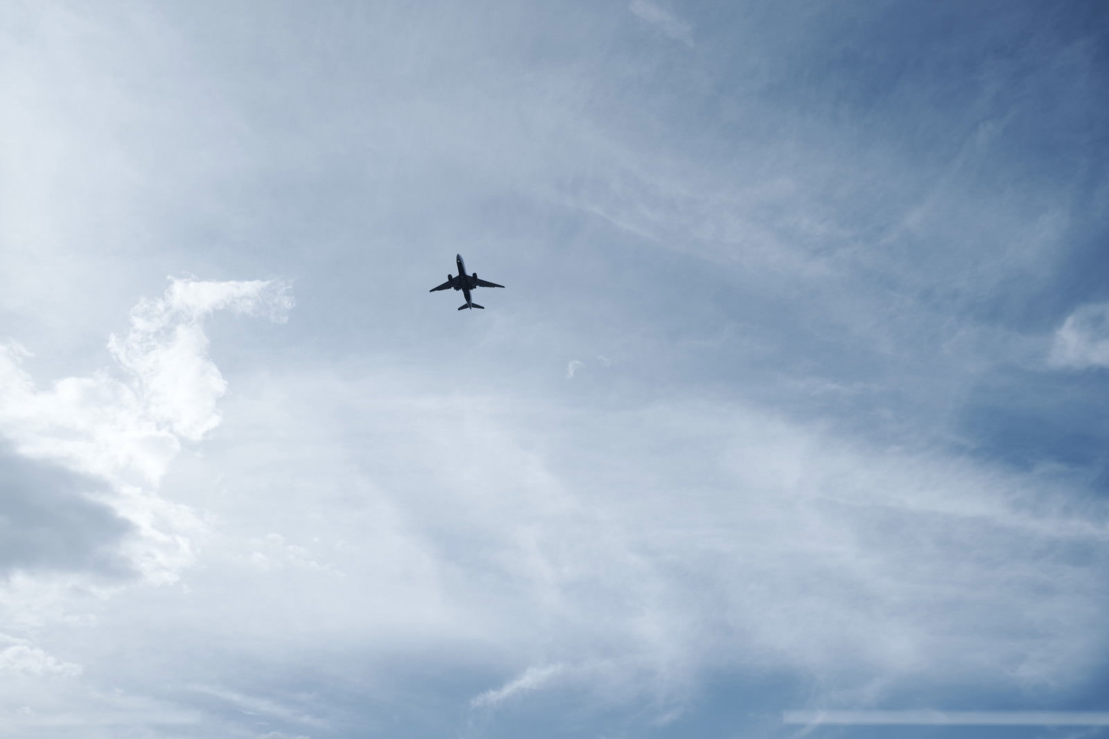 青空と雲を背景に飛行する大型旅客機のシルエット