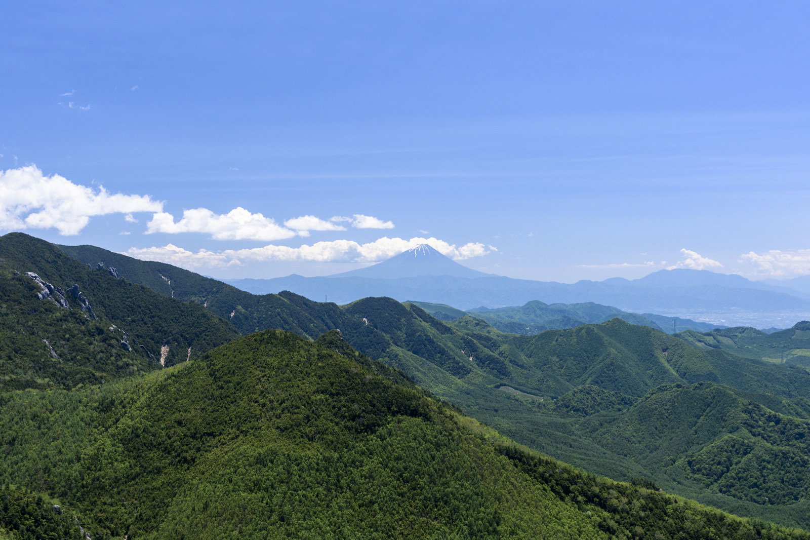 瑞牆山から望む富士山と青空に浮かぶ雲、緑の山々が連なるパノラマ風景
