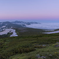 夜明けを迎える大雪山の稜線と朝焼けの空、トムラウシ山の雪渓の写真