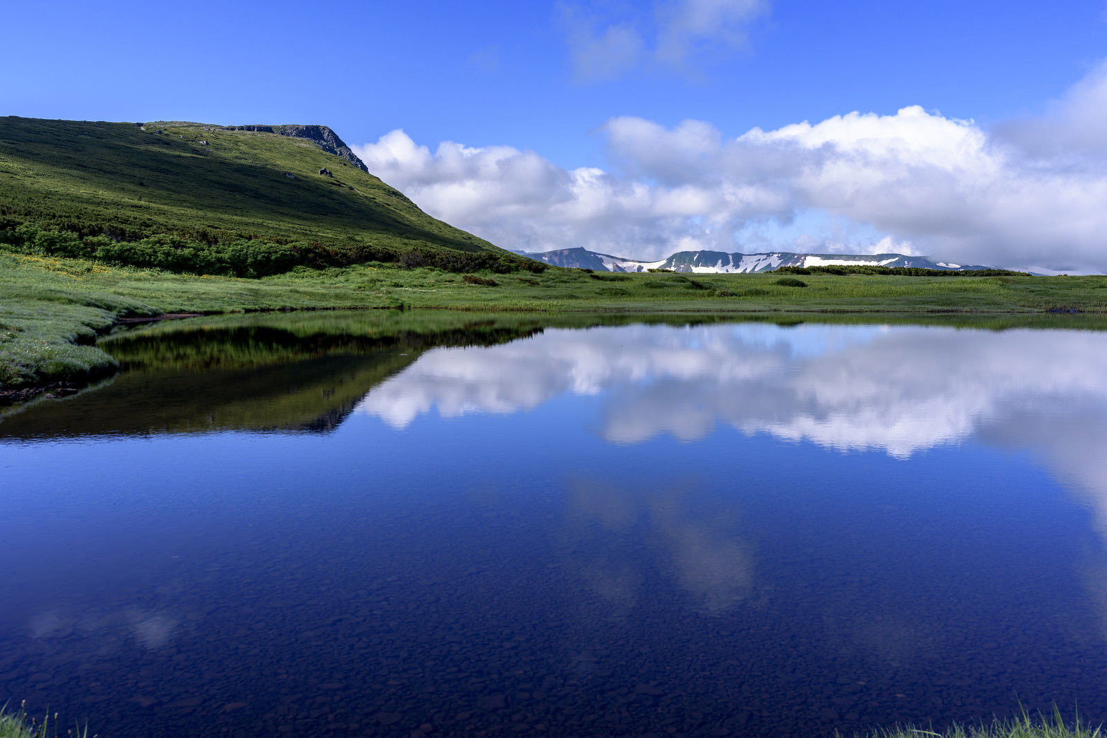 青空と雲、緑の山並みが水面に美しく映り込む忠別沼の水鏡風景