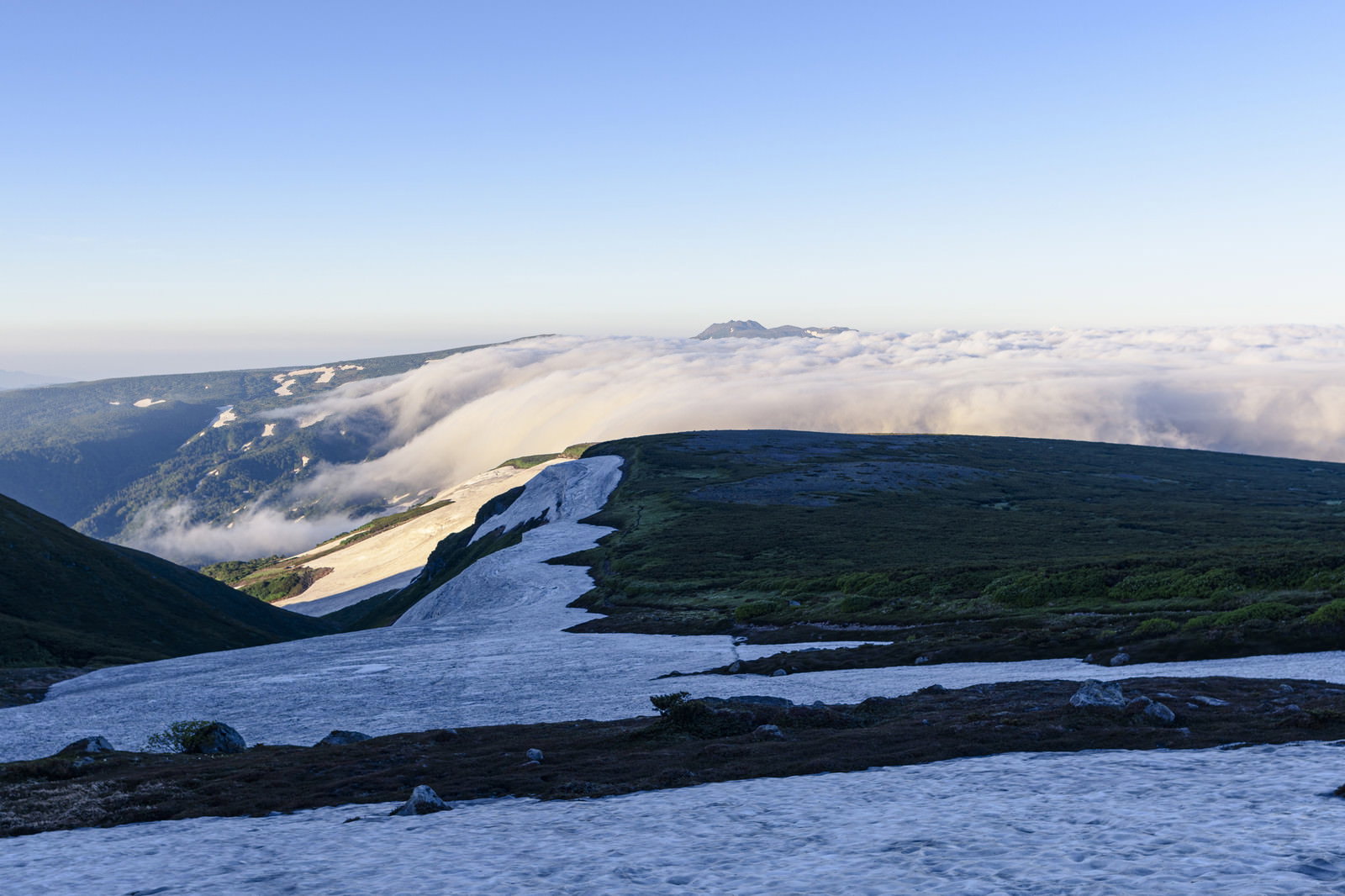 夕暮れ時の高根ヶ原で残雪と雲海が見える山岳風景