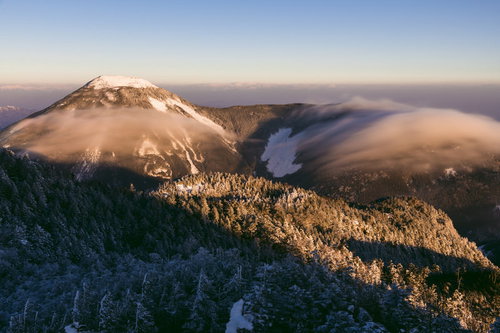 朝焼けに染まる冬の蓼科山、雪化粧した山頂を滝雲が流れる