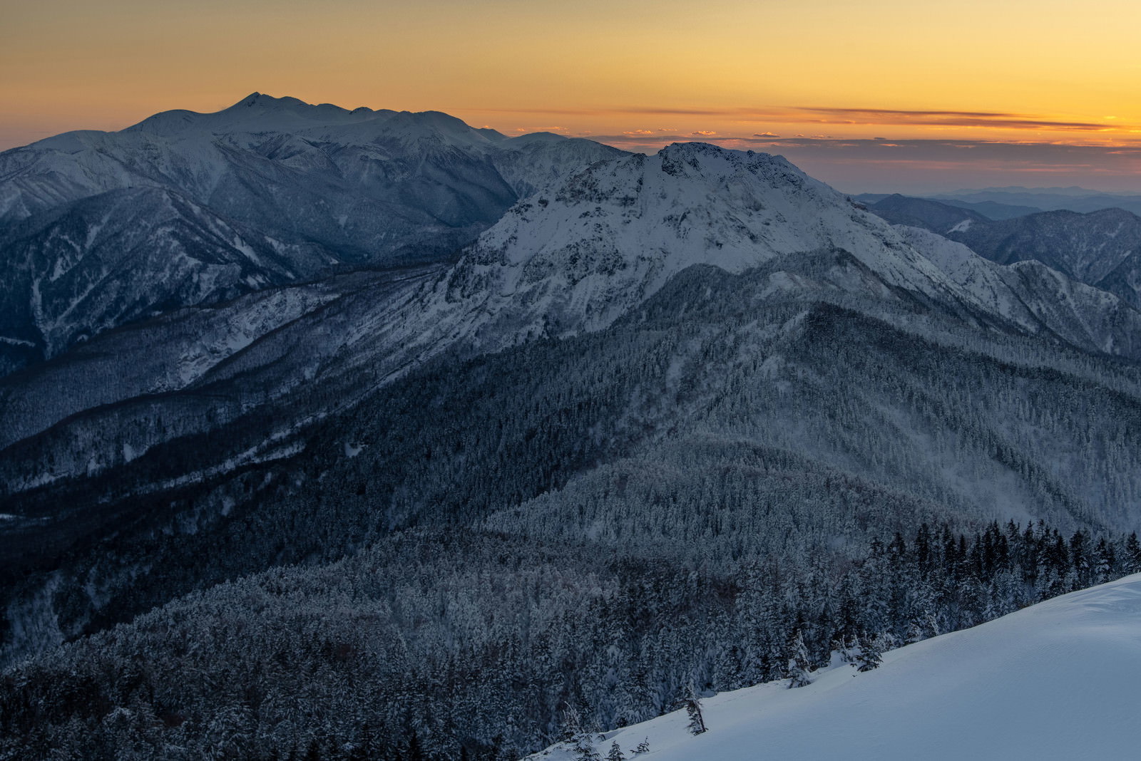 夕焼け空の下、雪化粧した乗鞍岳の山並みが連なる冬の山岳風景