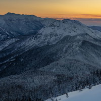 西穂高岳から見る夕焼けに染まる雪化粧の乗鞍岳の写真