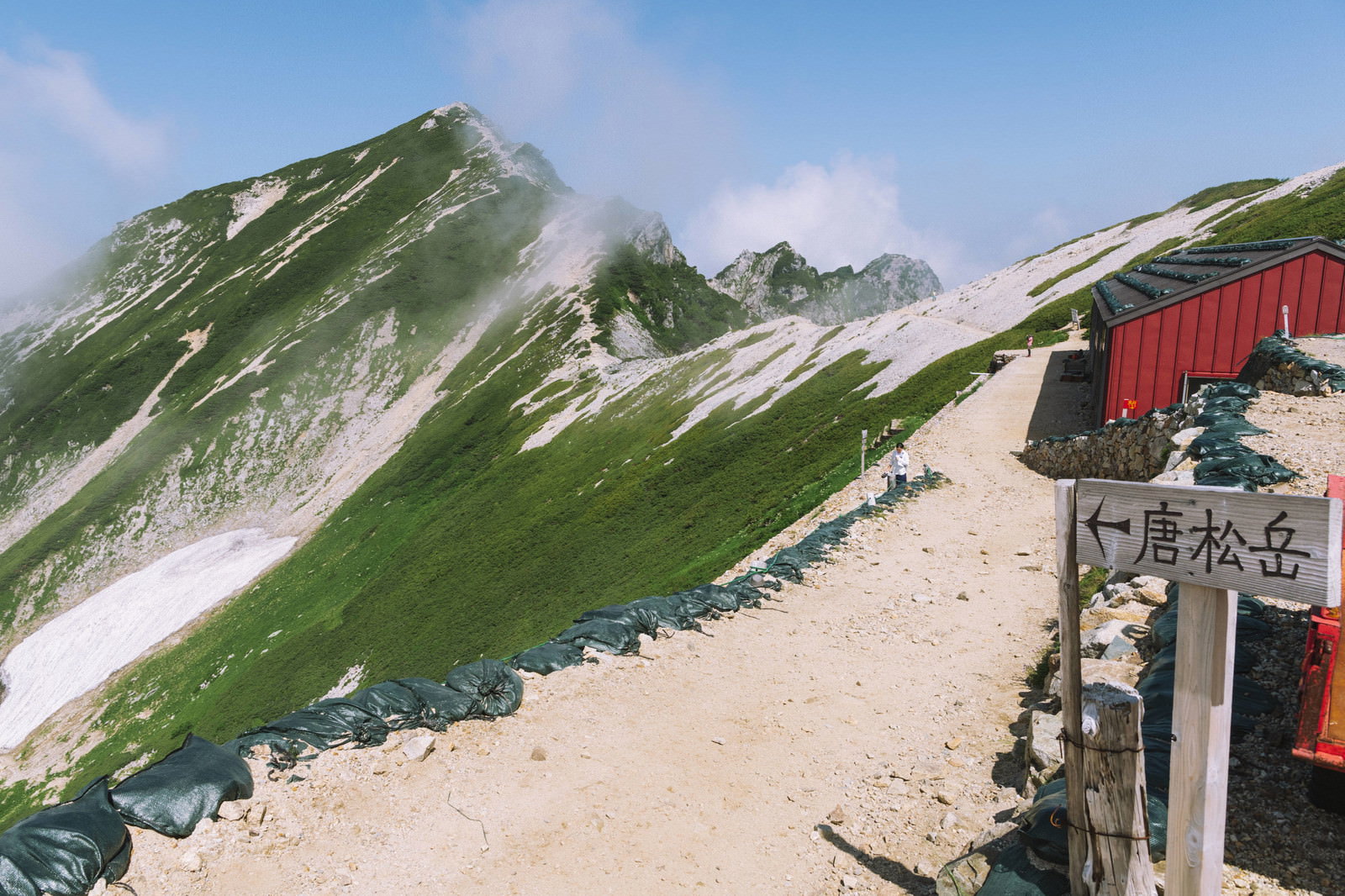 五竜岳と唐松岳を結ぶ稜線に建つ赤い屋根の山小屋と指導標