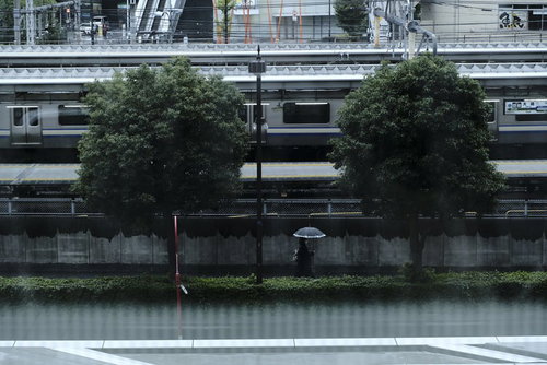 黒い傘をさして雨の歩道を歩く通行人の街並みを背景にした雨天時の風景