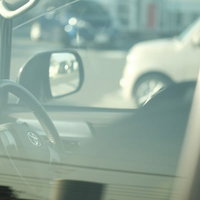 午後の駐車場の運転席でハンドルと窓ガラスが見える車内の写真