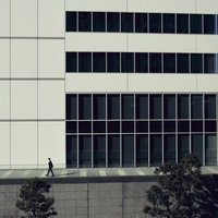 モダンなオフィスビルの前の歩道を歩くビジネスマンの写真