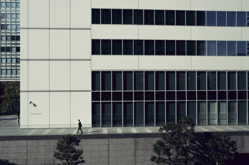 モダンなオフィスビルの前の歩道を歩くビジネスマン