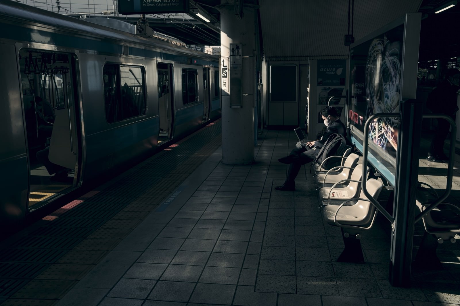 夕暮れの駅のホームで、ベンチに座って仕事をする人
