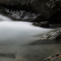 黒い岩肌を流れ落ちる白い渓流 長時間露光で撮影した滑らかな水流の写真