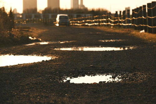 砂利敷きの道に点在する夕日に輝く水たまり