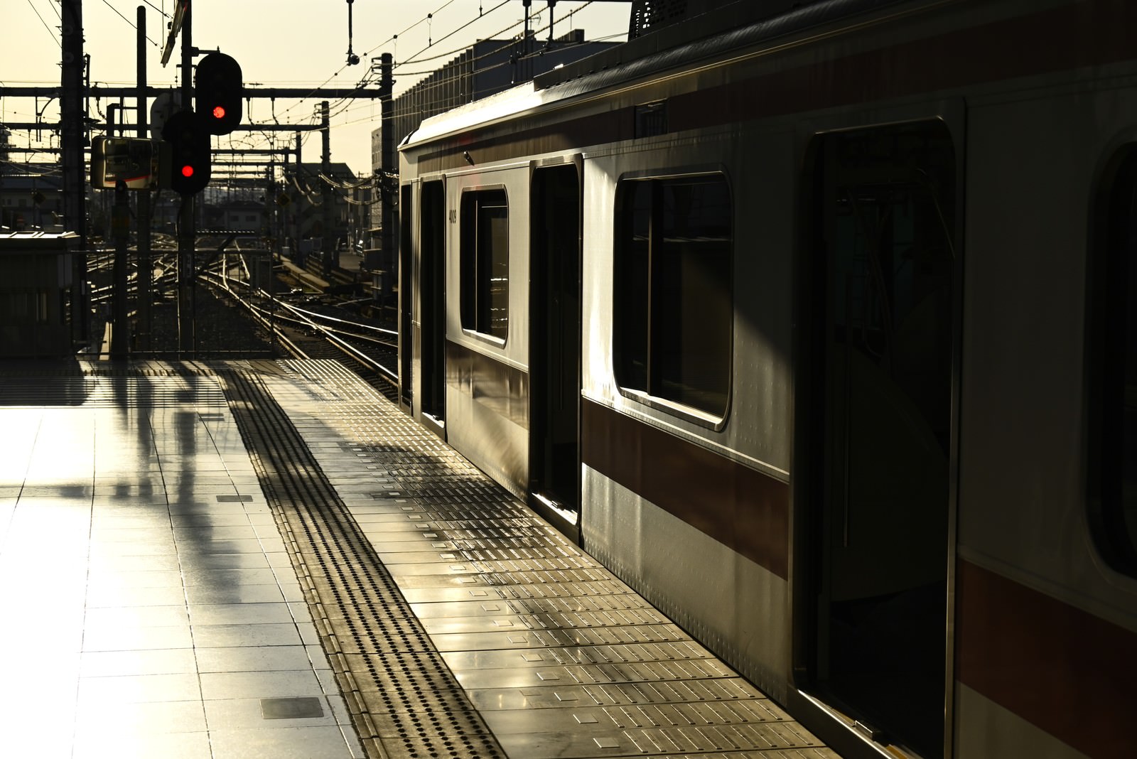朝日に照らされた駅ホームに停車している白い電車と信号機