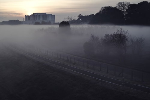 朝霧に包まれた河川敷に朝焼けでシルエットになる建物