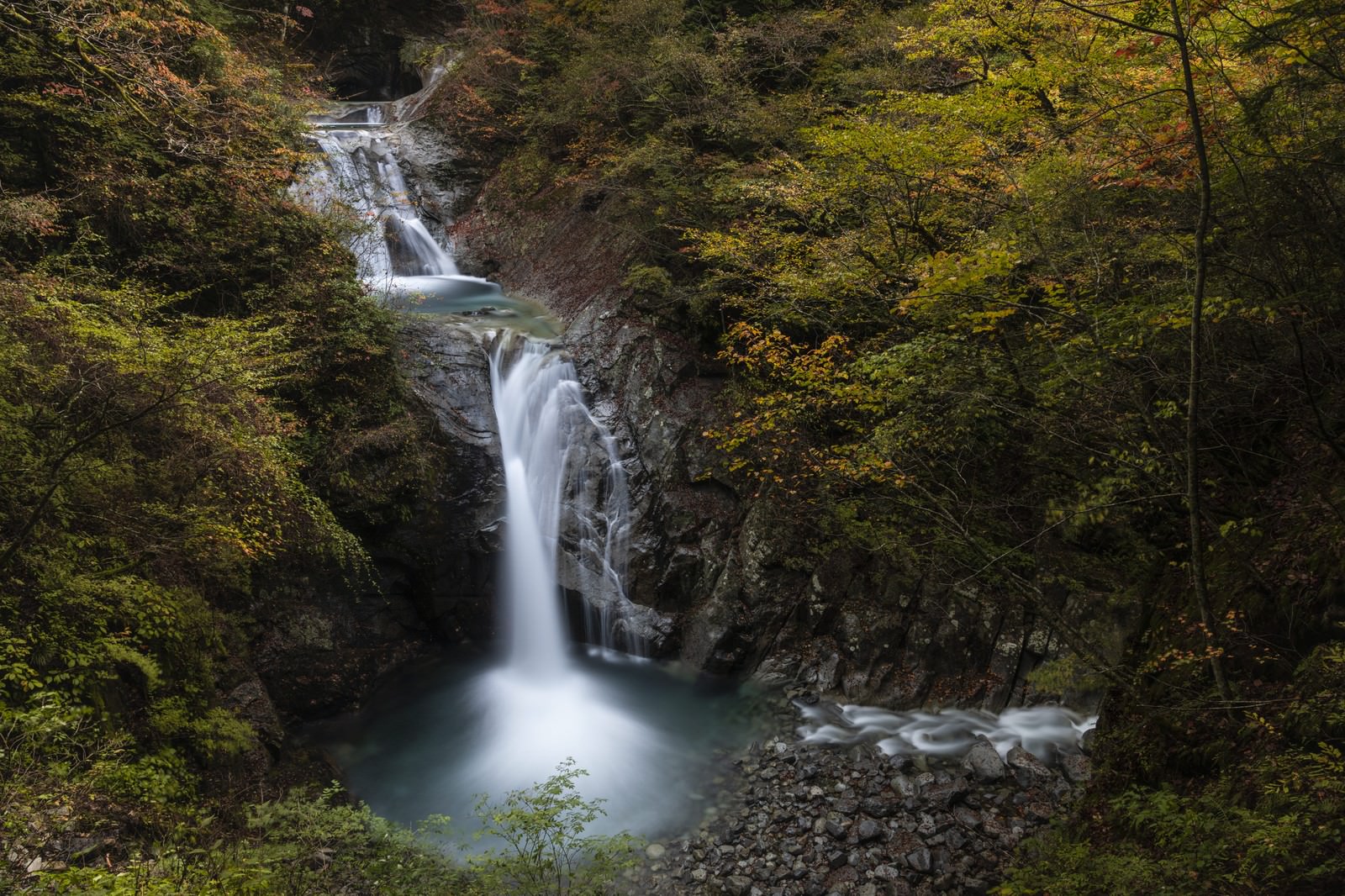 西沢渓谷の紅葉に囲まれた七ツ釜五段の滝が流れ落ちる様子