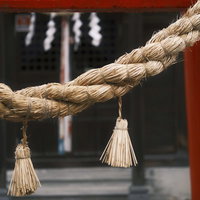 赤い鳥居に下げられた古びたしめ縄と白い房の写真