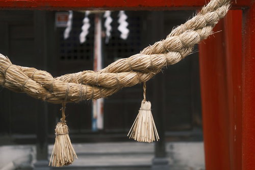 赤い鳥居に下げられた古びたしめ縄と白い房