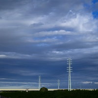 風に靡く雲と送電線のシルエット、曇り空に立つ鉄塔の写真