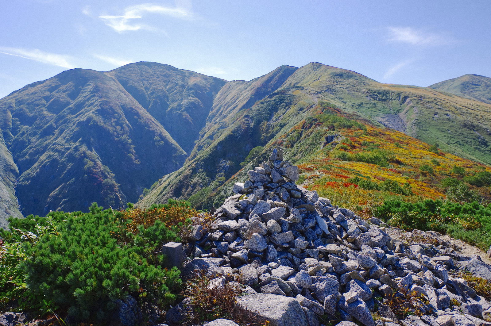 石を積み上げたケルンの向こうに緑の大朝日岳山頂が見える山岳風景