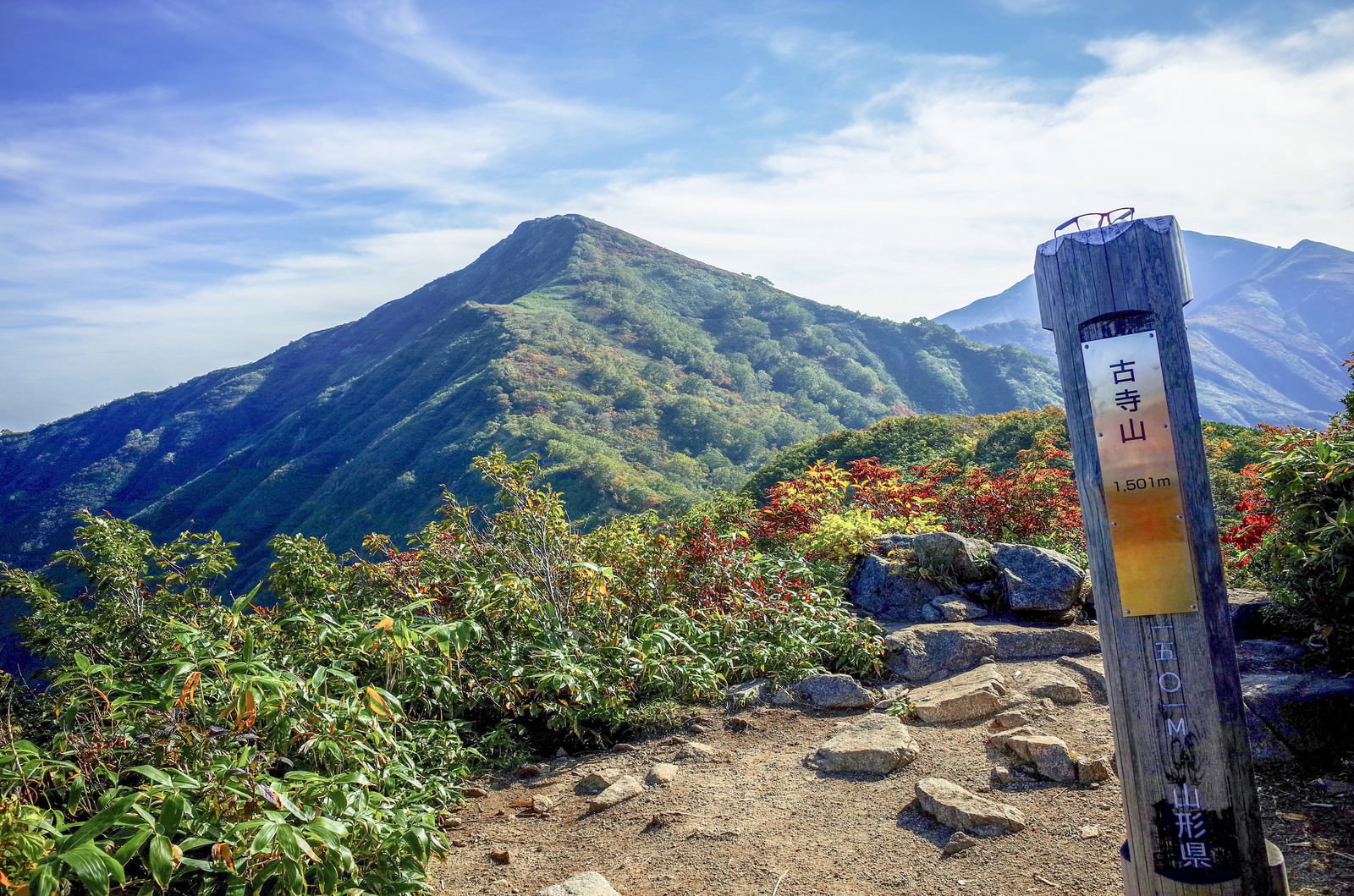 古寺山の山頂標越しに見る小朝日岳の山並みと青空