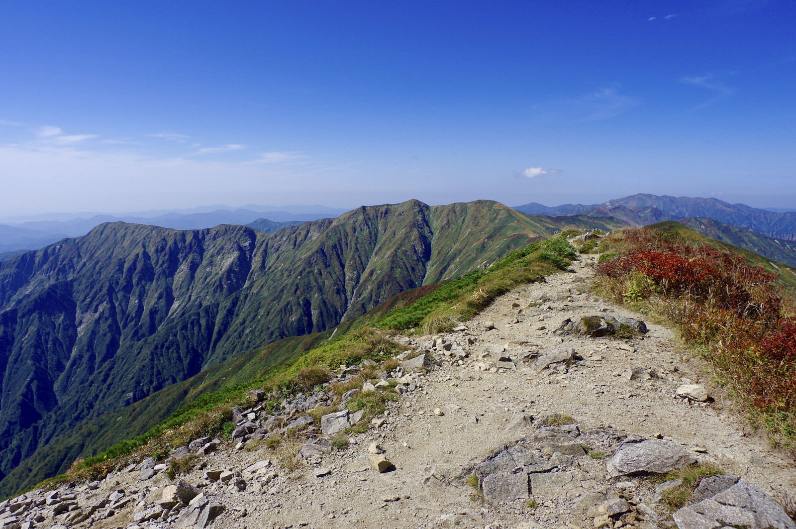 青空の下、大朝日岳の稜線に沿って続く岩場の登山道と連なる緑の山々