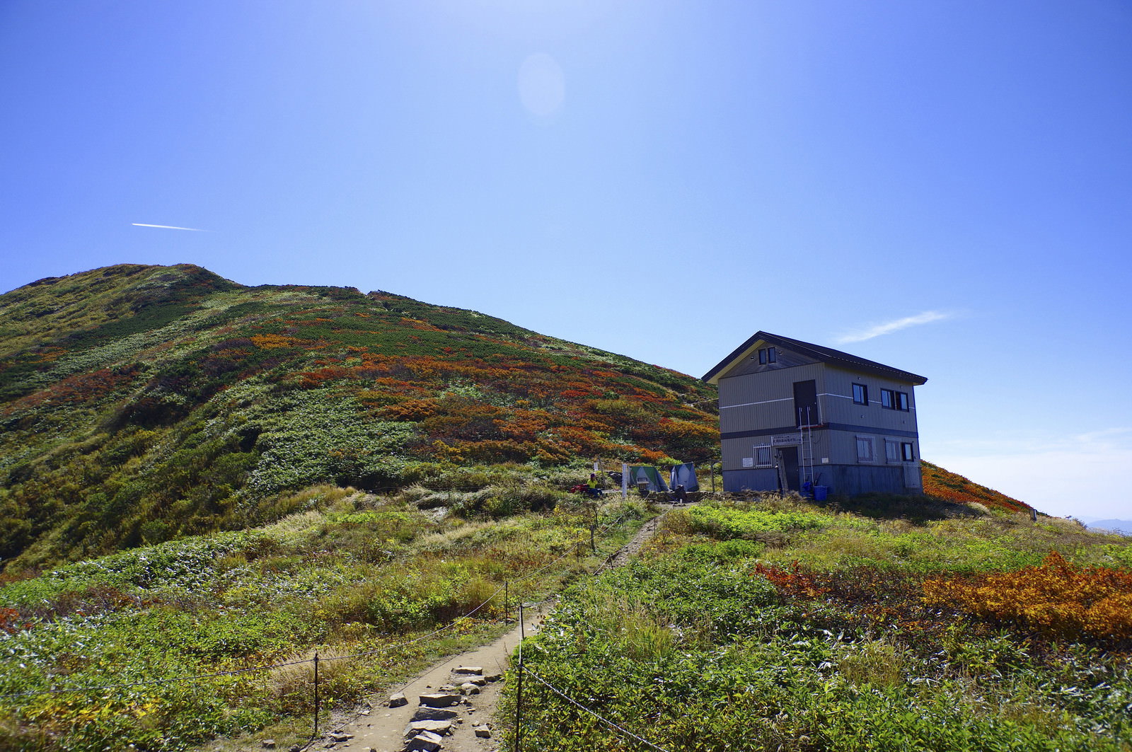 青空の下に建つ大朝日岳避難小屋と山頂方面に続く山稜線