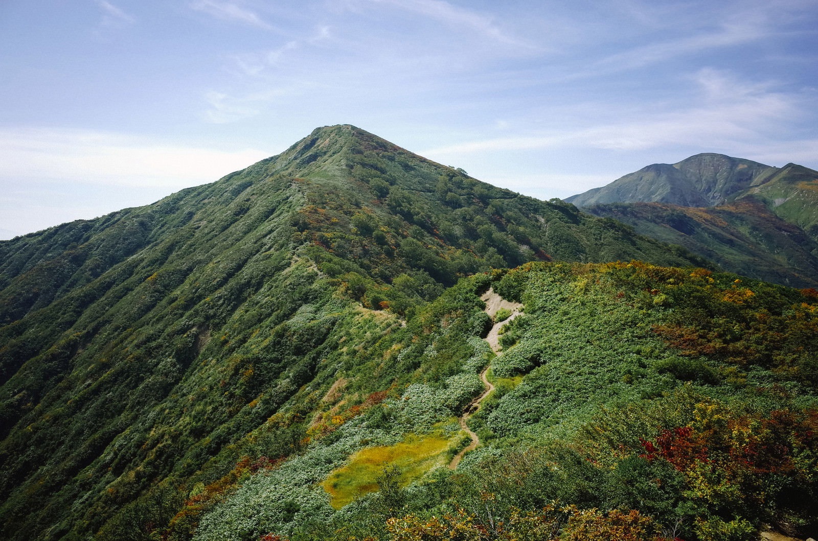 緑豊かな山々の稜線が続き、青空と白い雲が広がる大朝日岳から小朝日岳への眺望
