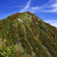 青空の下で紅葉に染まる小朝日岳（大朝日岳）の山容の写真