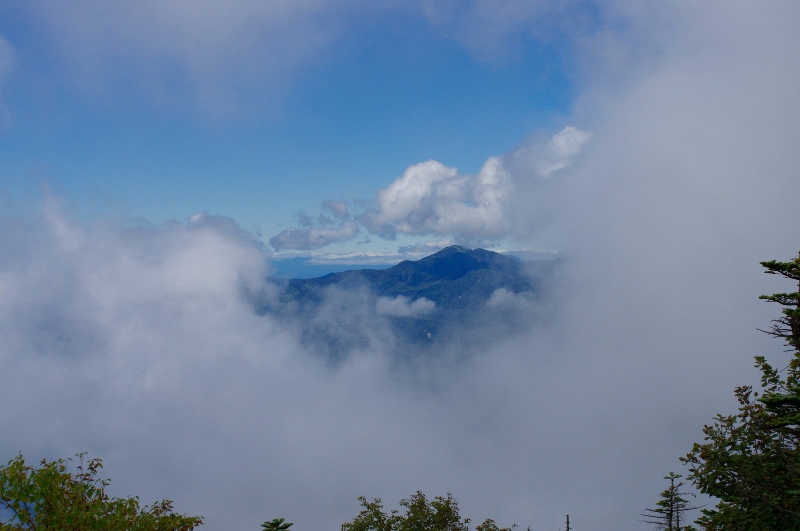 青空の下、白い雲海やガスに包まれた太郎山と男体山の山岳風景