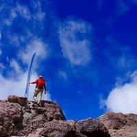 男体山の山頂で両手を上げて登頂を喜ぶ赤い服の登山者の写真