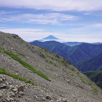 細かい石で流れそうな斜面と遠景の富士山（聖岳）の写真