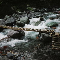 聖岳山中を流れる白い渓流とかけられた木製の橋の写真