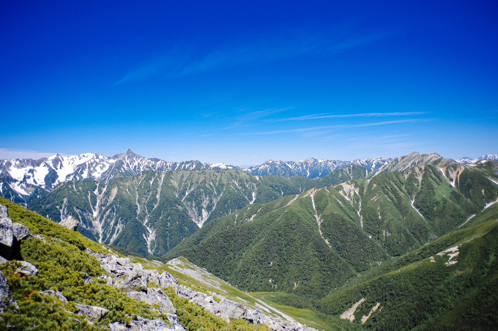 常念岳の山肌から槍ヶ岳方面の山脈を望む青空の下の雄大な景色