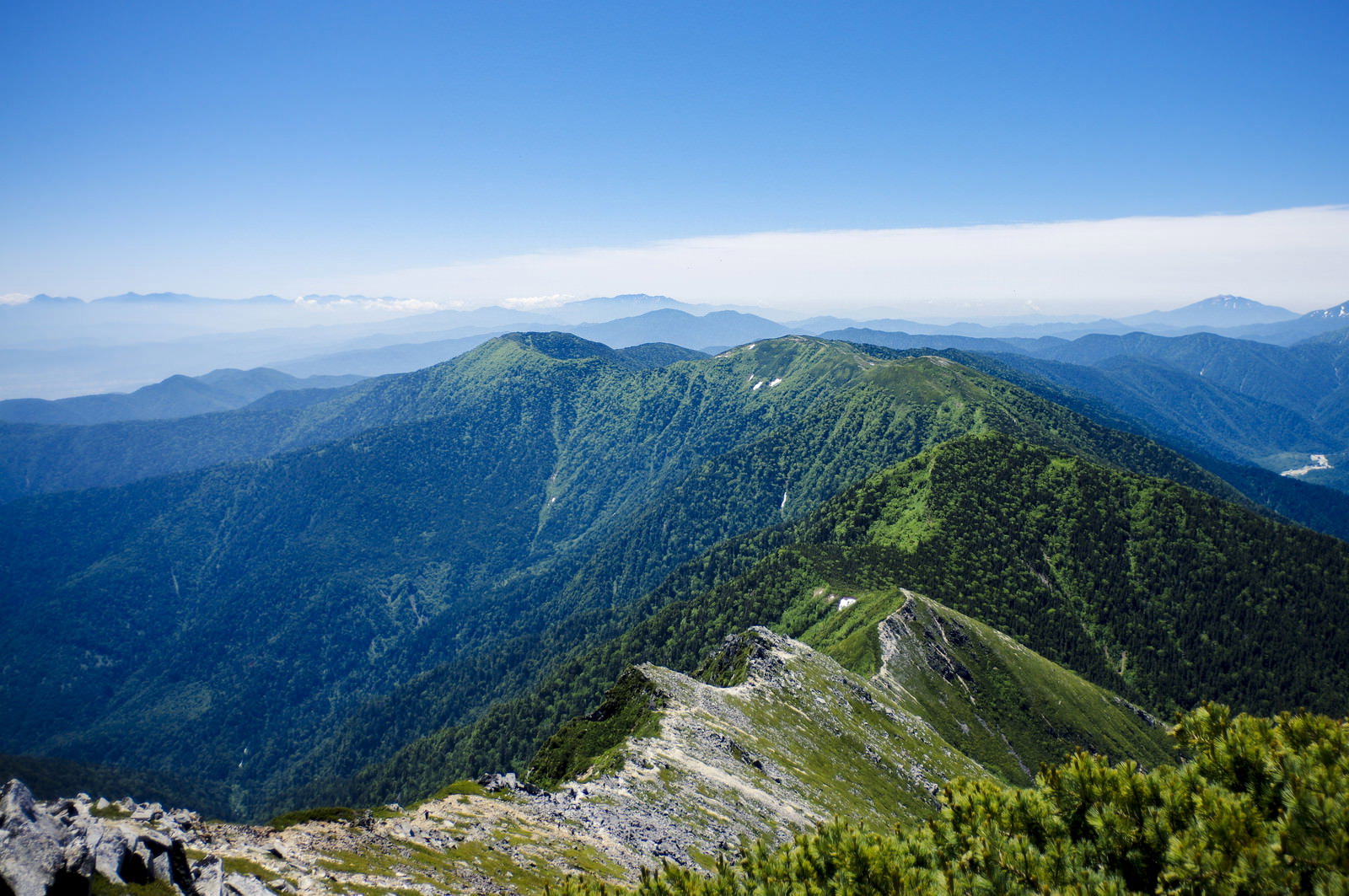 青空の下、常念岳へと続く登山道と緑の山肌、遠方に広がる山々の稜線