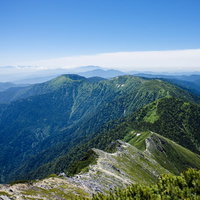 青空の下、常念岳へと続く登山道と山々の稜線の写真