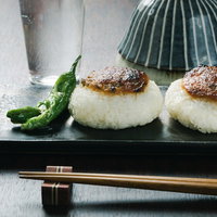 味噌のせ焼きおにぎりとししとう、黒い皿に盛られた温かい和食の写真