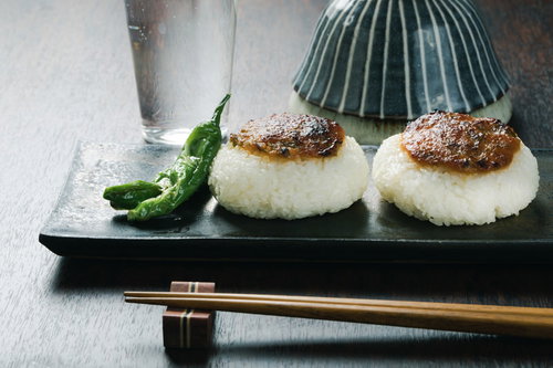 味噌のせ焼きおにぎりとししとう、黒い皿に盛られた温かい和食
