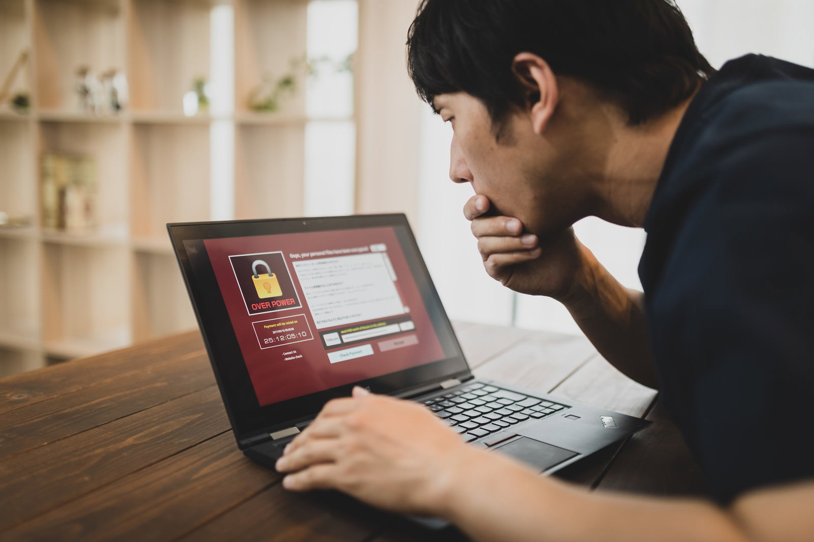 赤い警告画面とOVER POWERのテキストが表示されたパソコンを見つめる男性［モデル：大川竜弥］