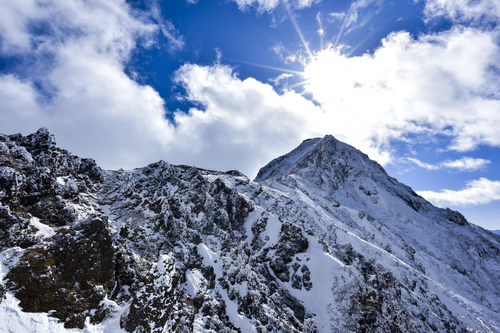 青空の下に雪化粧した険しい山々の稜線が連なる冬山の風景