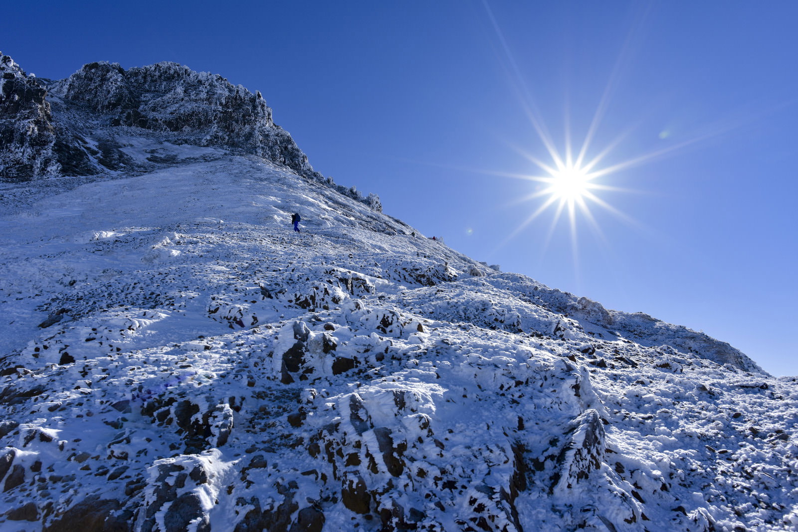 雪に覆われた文三郎尾根を登る登山者と青空に輝く太陽
