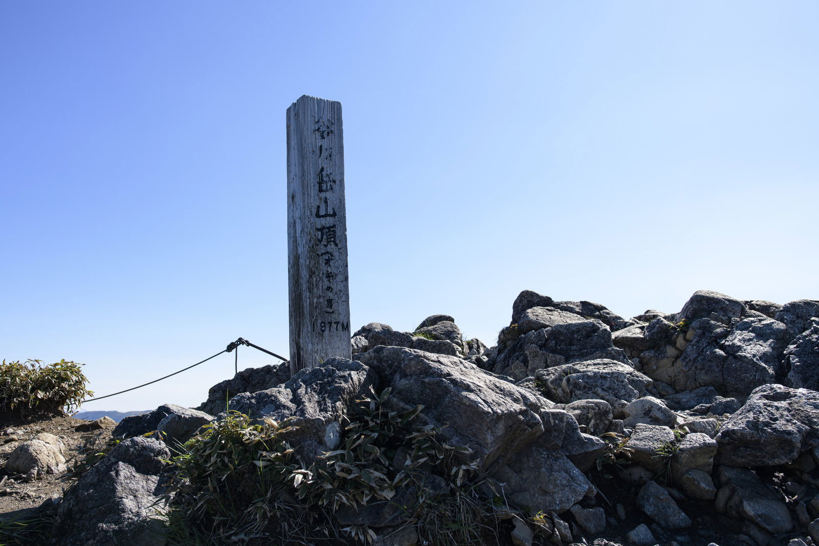 青空の下、岩場に立つ谷川岳オキの耳の山頂標と石積み