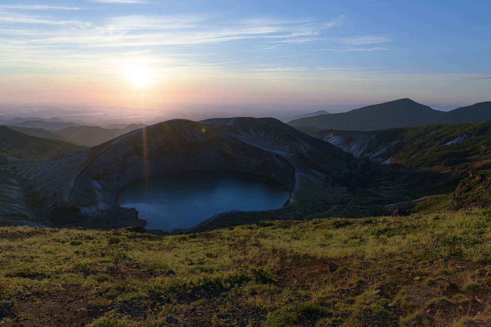 朝焼けの空の下、蔵王の山間にエメラルドグリーンのお釜が静かに佇む風景