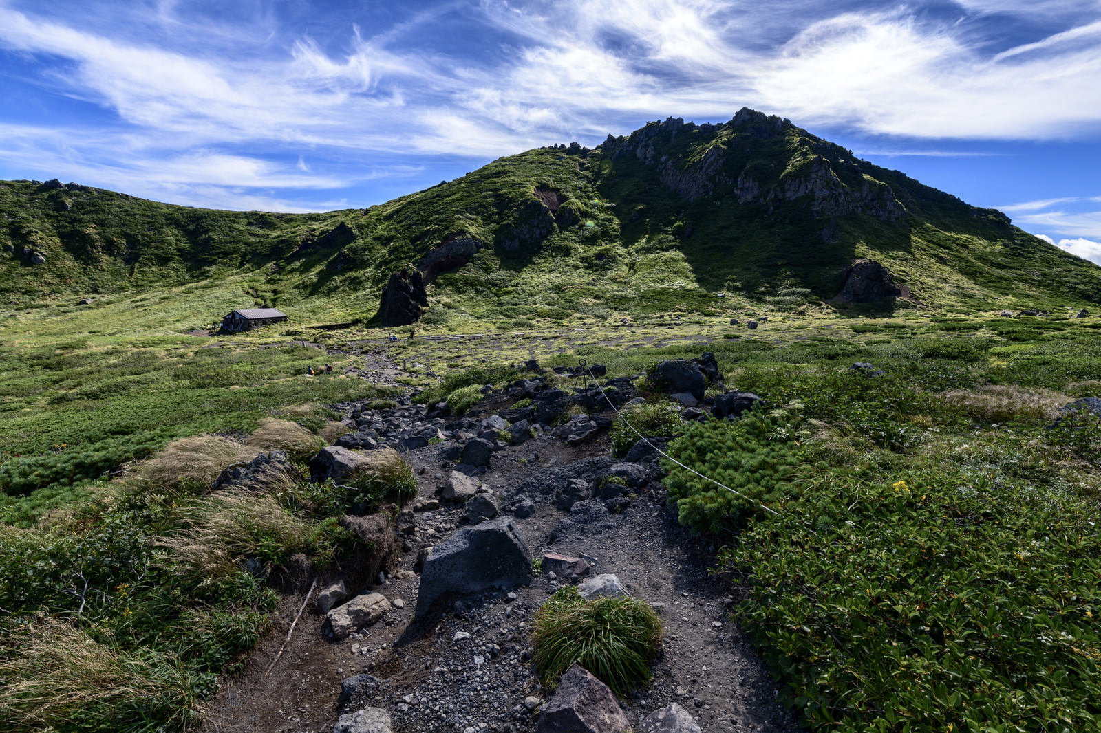 青空の下、緑の草原越しに岩手山を望む不動平の風景