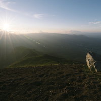 夕日の光芒に照らされる岩手山山頂の岩場と鬼ヶ城コース方面の写真