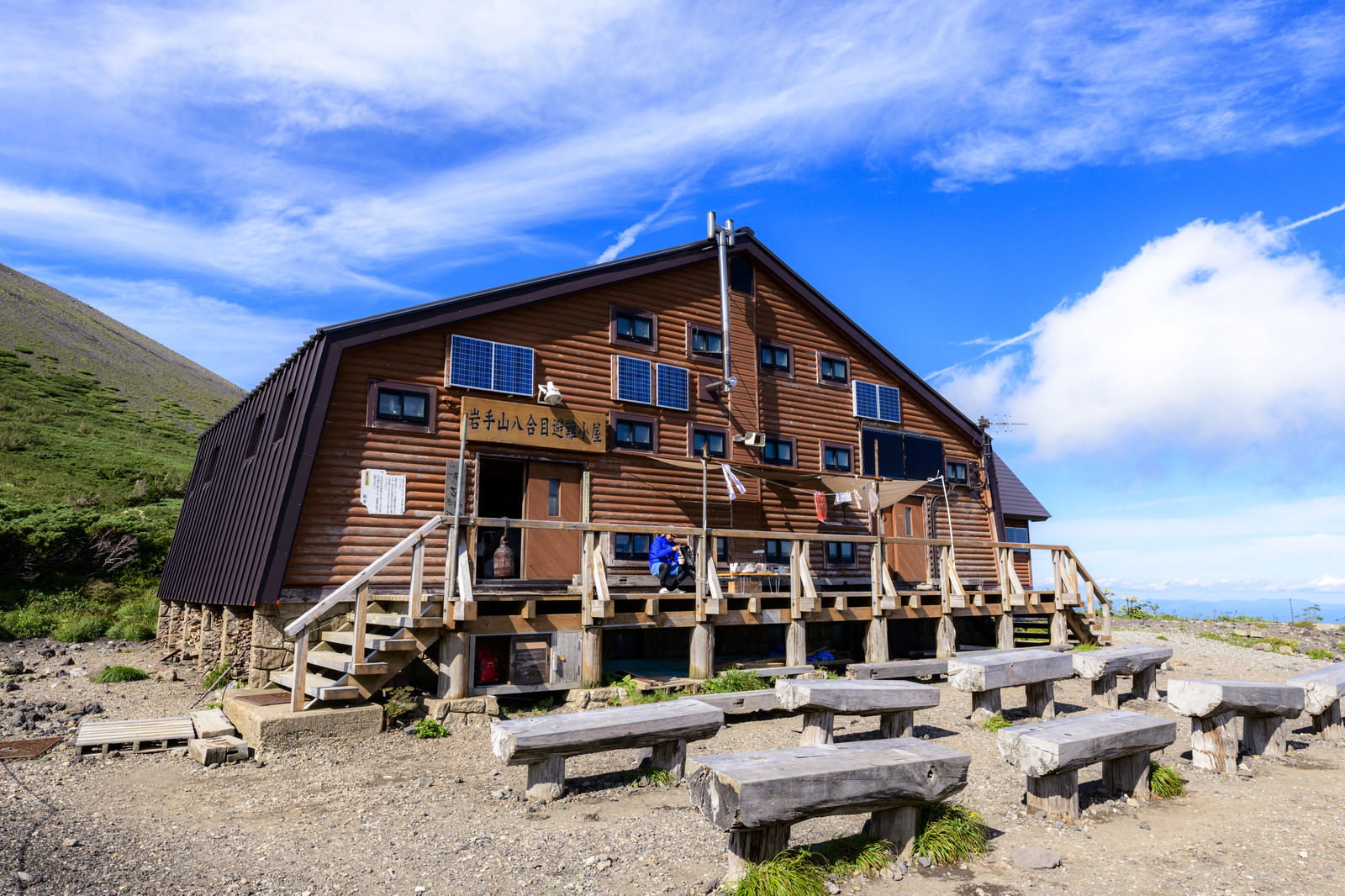 青空の下に建つ岩手山8合目小屋と休憩する登山者たち