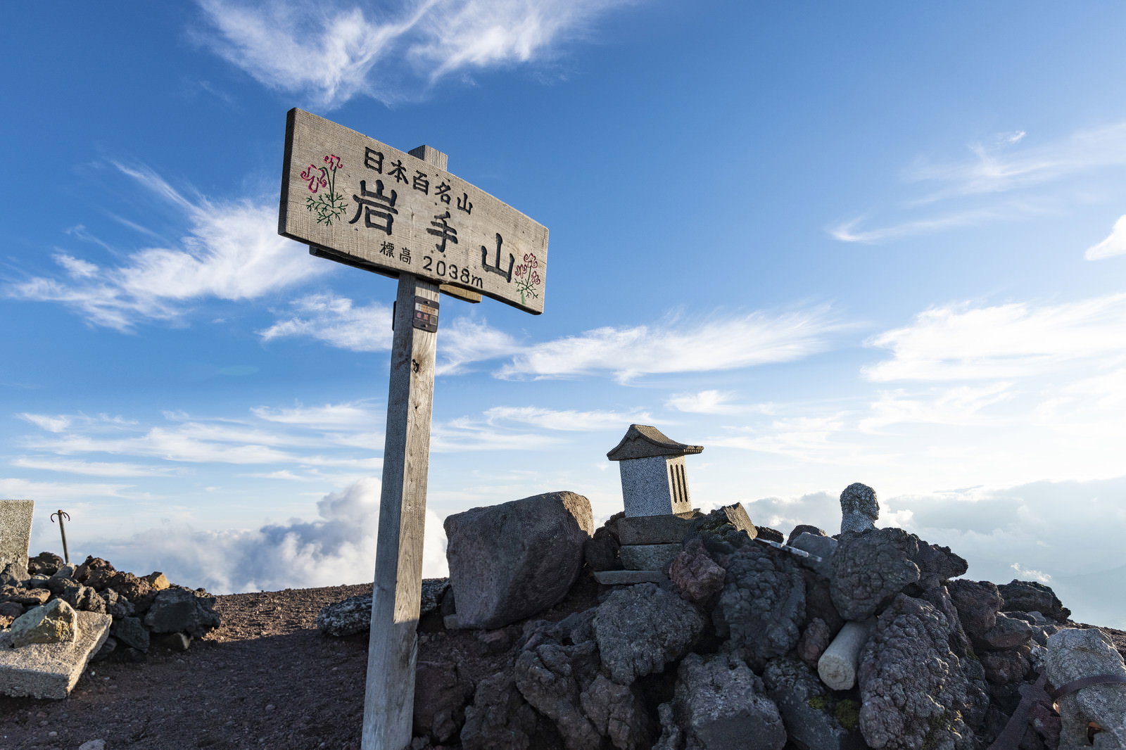 青空の下、岩手山山頂に立つ山頂碑と指導標