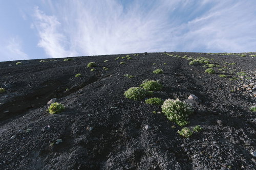 岩手山の火山斜面に広がる雲と青空、黒い火山岩と緑の低木